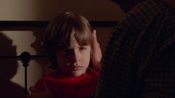 Movie still from “The Shining” (1980), directed by Stanley Kubrick – A young boy is being held up by a man; Close Up shot, Over the shoulder angle