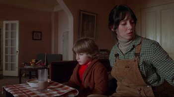Movie still from “The Shining” (1980), directed by Stanley Kubrick – A woman sitting next to a young boy at a table; Medium shot, Low angle