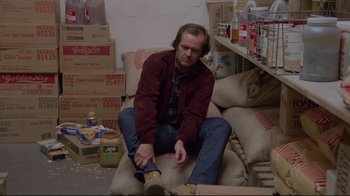 Movie still from “The Shining” (1980), directed by Stanley Kubrick – A man sitting on a couch in a room filled with boxes; Wide shot, High angle