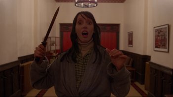 Movie still from “The Shining” (1980), directed by Stanley Kubrick – A woman is holding a knife in her hand and making a funny face; Medium shot, Low angle