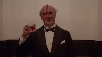 Movie still from “The Shining” (1980), directed by Stanley Kubrick – A man in a suit with a bloody face holding a glass of wine; Medium shot, Low angle