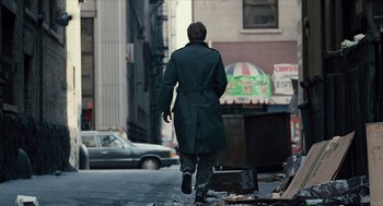 Movie still from “The Terminator” (1984), directed by James Cameron – A man walking down the street wearing a trench coat; Wide shot, Low angle