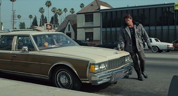 Movie still from “The Terminator” (1984), directed by James Cameron – A man standing in front of a parked car next to palm trees; Wide shot, Low angle