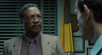 Movie still from “The Terminator” (1984), directed by James Cameron – An older man wearing a suit and tie talking to someone; Close Up shot, Over the shoulder angle