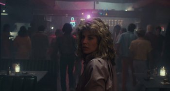 Movie still from “The Terminator” (1984), directed by James Cameron – A woman with a blonde wig standing in front of a group of people; Medium shot, Low angle