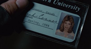 Movie still from “The Terminator” (1984), directed by James Cameron – A person holding a name tag with a picture of a woman; Extreme Close Up shot, Overhead angle