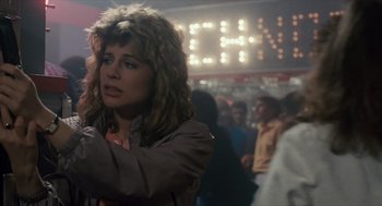 Movie still from “The Terminator” (1984), directed by James Cameron – A woman with a messy hair style standing in front of a group of people; Close Up shot, Over the shoulder angle