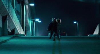Movie still from “The Terminator” (1984), directed by James Cameron – Two people are running on a bridge at night; Wide shot, Low angle