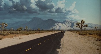 Movie still from “The Terminator” (1984), directed by James Cameron – A car driving down the middle of a desert road; Extreme Wide shot, High angle
