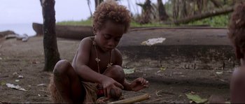 Movie still from “The Thin Red Line” (1998), directed by Terrence Malick – A young child is playing with a stick; Close Up shot, High angle