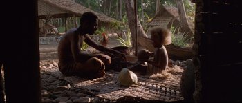 Movie still from “The Thin Red Line” (1998), directed by Terrence Malick – A man and a child sitting on the ground; Wide shot, High angle