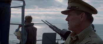 Movie still from “The Thin Red Line” (1998), directed by Terrence Malick – A man in a hat is standing next to a boat; Medium shot, Over the shoulder angle