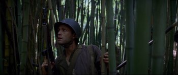 Movie still from “The Thin Red Line” (1998), directed by Terrence Malick – A man wearing a helmet standing in the middle of a forest; Medium shot, Low angle