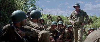Movie still from “The Thin Red Line” (1998), directed by Terrence Malick – A group of men sitting on top of a grass covered field; Wide shot, Low angle