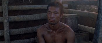 Movie still from “The Thin Red Line” (1998), directed by Terrence Malick – A shirtless man sitting in front of a wooden structure; Close Up shot, High angle