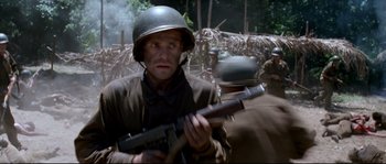 Movie still from “The Thin Red Line” (1998), directed by Terrence Malick – A man holding a gun while standing next to another man; Medium shot, Low angle
