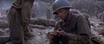 Movie still from “The Thin Red Line” (1998), directed by Terrence Malick – A man in a military uniform is looking at his cell phone; Close Up shot, High angle