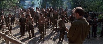Movie still from “The Thin Red Line” (1998), directed by Terrence Malick – A large group of men standing next to each other; Wide shot, Over the shoulder angle