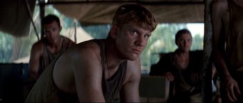 Movie still from “The Thin Red Line” (1998), directed by Terrence Malick – A young man with blond hair is sitting down; Close Up shot, Over the shoulder angle