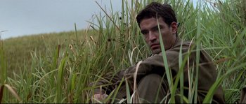 Movie still from “The Thin Red Line” (1998), directed by Terrence Malick – A man sitting in tall grass in a field; Close Up shot, Over the shoulder angle