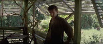 Movie still from “The Thin Red Line” (1998), directed by Terrence Malick – A man standing on a bench near a tree; Medium shot, Low angle