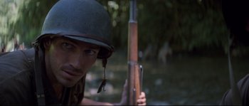 Movie still from “The Thin Red Line” (1998), directed by Terrence Malick – A man with a helmet and a rifle; Close Up shot, High angle