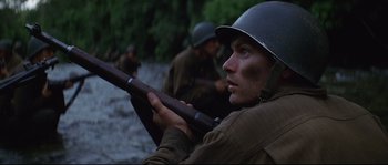 Movie still from “The Thin Red Line” (1998), directed by Terrence Malick – A man holding a rifle while standing next to other men; Close Up shot, Low angle