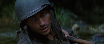 Movie still from “The Thin Red Line” (1998), directed by Terrence Malick – A man wearing a helmet is looking into the camera; Close Up shot, High angle