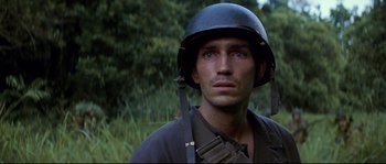 Movie still from “The Thin Red Line” (1998), directed by Terrence Malick – A man wearing a helmet and holding a rifle; Close Up shot, Over the shoulder angle