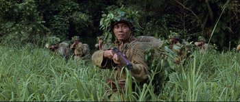 Movie still from “The Thin Red Line” (1998), directed by Terrence Malick – A man in a military uniform is holding a rifle; Medium shot, Over the shoulder angle