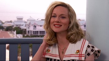 Movie still from “The Truman Show” (1998), directed by Peter Weir – A woman sitting on a bench smiling for the camera; Close Up shot, Over the shoulder angle