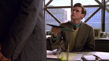 Movie still from “The Truman Show” (1998), directed by Peter Weir – A man in a suit and tie holding a paper plane; Medium shot, Over the shoulder angle