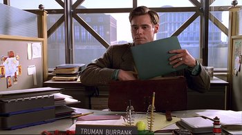 Movie still from “The Truman Show” (1998), directed by Peter Weir – A man sitting at a desk holding a file; Medium shot, Low angle