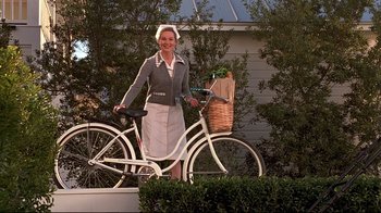 Movie still from “The Truman Show” (1998), directed by Peter Weir – A woman standing next to a bike with a basket on it; Wide shot, Low angle