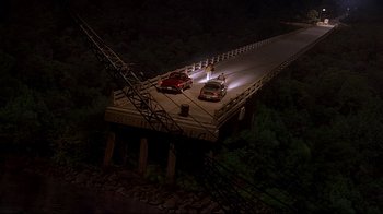 Movie still from “The Truman Show” (1998), directed by Peter Weir – A car is driving over a bridge at night; Extreme Wide shot, High angle