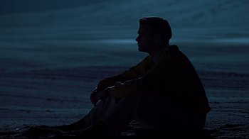 Movie still from “The Truman Show” (1998), directed by Peter Weir – A man sitting on the ground in the dark at night; Wide shot, Over the shoulder angle