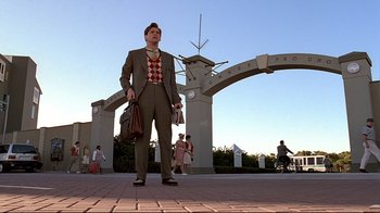 Movie still from “The Truman Show” (1998), directed by Peter Weir – A man is standing on the sidewalk holding a bag; Wide shot, Low angle