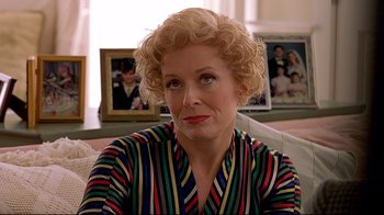 Movie still from “The Truman Show” (1998), directed by Peter Weir – An older woman with blonde curly hair wearing a colorful striped shirt; Close Up shot, Over the shoulder angle