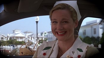 Movie still from “The Truman Show” (1998), directed by Peter Weir – A woman in a nurse's outfit smiles in the backseat of a car; Close Up shot, Low angle
