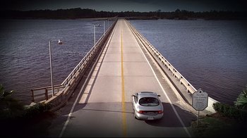 Movie still from “The Truman Show” (1998), directed by Peter Weir – A white car driving on a bridge over a river; Extreme Wide shot, High angle
