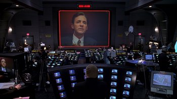 Movie still from “The Truman Show” (1998), directed by Peter Weir – A man sitting in front of a large screen tv; Medium shot, High angle