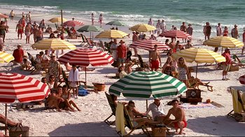 Movie still from “The Truman Show” (1998), directed by Peter Weir – Many people are sitting and standing on the beach under striped umbrellas; Extreme Wide shot, High angle