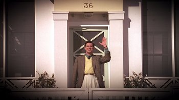 Movie still from “The Truman Show” (1998), directed by Peter Weir – A man waving at the camera in front of a house; Wide shot, Low angle