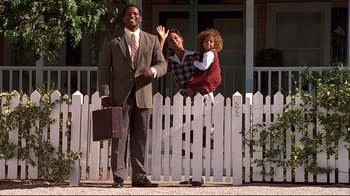 Movie still from “The Truman Show” (1998), directed by Peter Weir – A man and a woman and a little girl standing in front of a white picket fence; Wide shot, Low angle