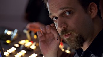 Movie still from “The Truman Show” (1998), directed by Peter Weir – A man with a beard is holding his hand up to his ear; Close Up shot, Low angle