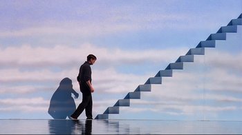 Movie still from “The Truman Show” (1998), directed by Peter Weir – A man is walking up a set of stairs; Extreme Wide shot, Low angle