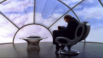 Movie still from “The Truman Show” (1998), directed by Peter Weir – A man sitting on a chair in front of a futuristic chair; Wide shot, Low angle