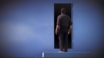 Movie still from “The Truman Show” (1998), directed by Peter Weir – A man standing on a platform in front of an open door; Wide shot, Low angle