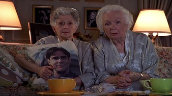 Movie still from “The Truman Show” (1998), directed by Peter Weir – Two older women sitting next to each other holding pillows; Medium shot, High angle
