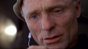 Movie still from “The Truman Show” (1998), directed by Peter Weir – An older man holding a pair of ear buds; Extreme Close Up shot, Low angle